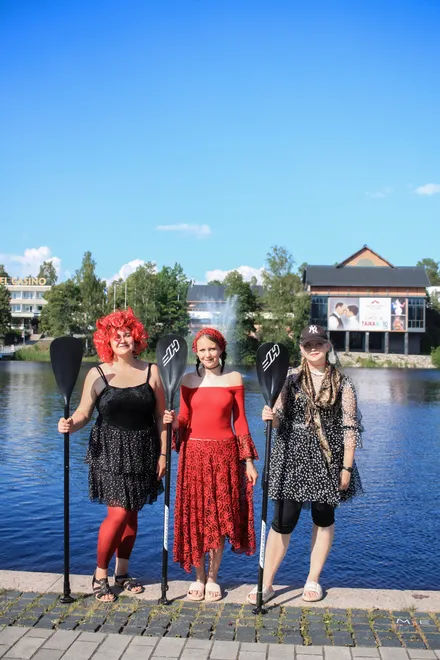 Three festival participants in bright costumes with the lake in the background
