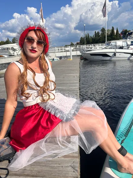A bright participant in a Little Red Riding Hood costume sitting on a pier with the lake in the background.